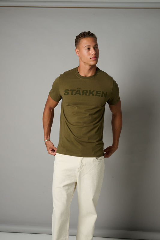 Man wearing a green t-shirt with 'Stärken' text against a gray background